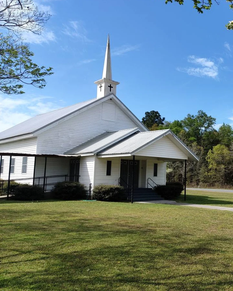 The white Beulah Baptist Church building, entrance, and steeple beneath live oak branches
